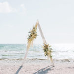 White washed A frame arbor with boho inspired fresh flower arrangements out on the sandy beach